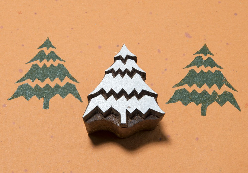A wooden pottery stamp with a Christmas tree design, showcasing the silhouette of a tree with detailed line patterns on its branches, placed on an orange background.